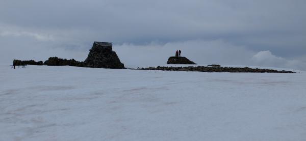 Photo of Snow still present at summit of Ben Nevis. Left to right: Ruined observatory, emergency shelter, trig point